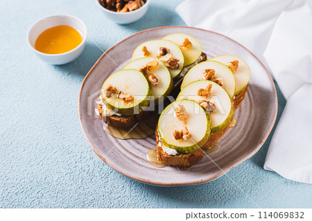 Pieces of pear, ricotta, honey and nuts on rye bruschettas on a plate on the table 114069832
