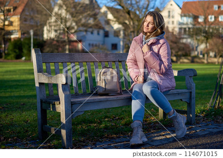 Winter Wonderland Elegance: Beautiful Girl in Pink Jacket Enjoys Festive Atmosphere in Bitigheim-Bissingen Park. girl in a pink winter jacket sits on a bench in a park against the backdrop of the Winter Wonderland Elegance: Beautiful Girl in Pink Jacket Enjoys Festive Atmosphere in Bitigheim-Bissingen Park. girl in a pink winter jacket sits on a bench in a park against the backdrop of the 114071015