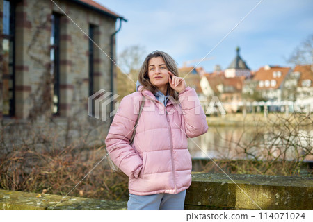 Young beautiful pretty tourist girl in warm hat and coat with backpack walking at cold autumn in Europe city enjoying her travel in Bietigheim-Bissingen, Deutschland. Outdoor portrait of young tourist Young beautiful pretty tourist girl in warm hat and coat with backpack walking at cold autumn in Europe city enjoying her travel in Bietigheim-Bissingen, Deutschland. Outdoor portrait of young tourist 114071024