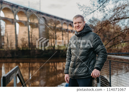 Timeless Elegance: 40-Year-Old Man in Stylish Jacket by Neckar River and Historic Bridge in Bietigheim-Bissingen, Germany Timeless Elegance: 40-Year-Old Man in Stylish Jacket by Neckar River and Historic Bridge in Bietigheim-Bissingen, Germany 114071067