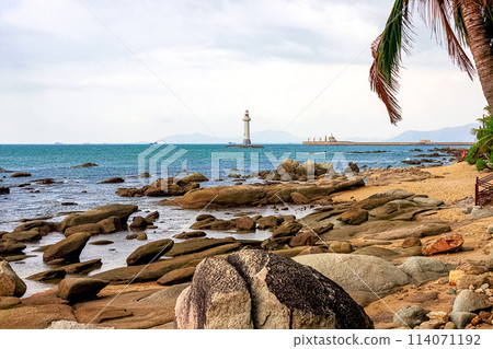 View of a lighthouse in the sea near a rocky shore with palm trees. Heavenly Grottoes Park, Sanya. View of a lighthouse in the sea near a rocky shore with palm trees. Heavenly Grottoes Park, Sanya. 114071192