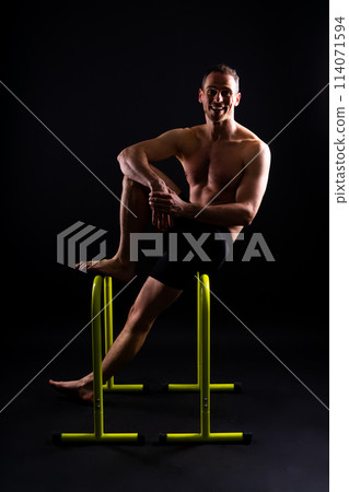 Front and side view photo of an strong young man exercising on parallel bars in studio. Front and side view photo of an strong young man exercising on parallel bars in studio. 114071594