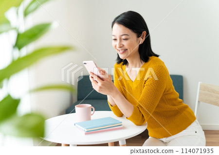 A middle-aged woman wearing earphones and looking at her smartphone 114071935
