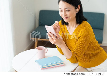A middle-aged woman wearing earphones and looking at her smartphone 114071938