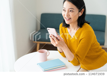 A middle-aged woman wearing earphones and looking at her smartphone A middle-aged woman wearing earphones and looking at her smartphone 114071939