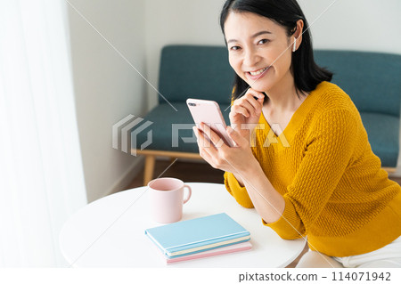 A middle-aged woman wearing earphones and looking at her smartphone A middle-aged woman wearing earphones and looking at her smartphone 114071942