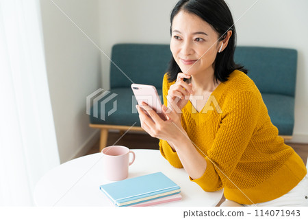 A middle-aged woman wearing earphones and looking at her smartphone A middle-aged woman wearing earphones and looking at her smartphone 114071943