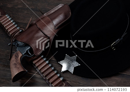Sheriff star badge with gun, holster and gun belt with old west hat on table. Top view. Sheriff star badge with gun, holster and gun belt with old west hat on table. Top view. 114072193