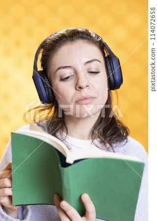 Woman concentrating on reading book, relaxing and listening audio white noise, isolated over studio background. Geek with novel in hand hearing songs through headphones, entertainment concept Woman concentrating on reading book, relaxing and listening audio white noise, isolated over studio background. Geek with novel in hand hearing songs through headphones, entertainment concept 114072658