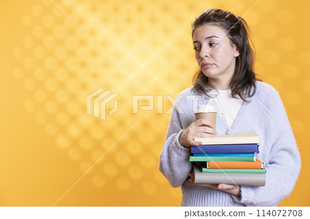 Portrait of woman with stack of books in hands holding disposable cup of coffee, isolated over studio background. Bookworm holding pile of novels and caffeinated drink early in the morning Portrait of woman with stack of books in hands holding disposable cup of coffee, isolated over studio background. Bookworm holding pile of novels and caffeinated drink early in the morning 114072708