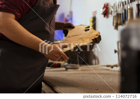 Carpenter holding timber block, doing quality assurance on it before starting furniture assembling in workshop, close up shot. Manufacturer in joinery preparing piece of wood for carving Carpenter holding timber block, doing quality assurance on it before starting furniture assembling in workshop, close up shot. Manufacturer in joinery preparing piece of wood for carving 114072716