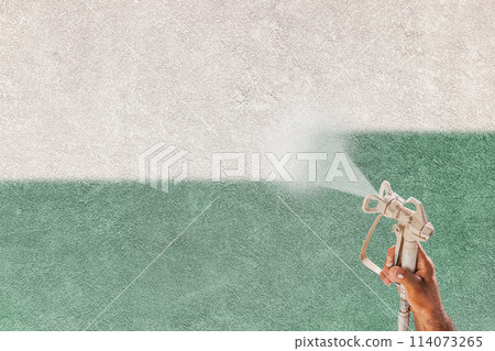 Professional Spray Painter Holding Spray Gun Spraying White Paint Over Teal Stucco Surface. 114073265