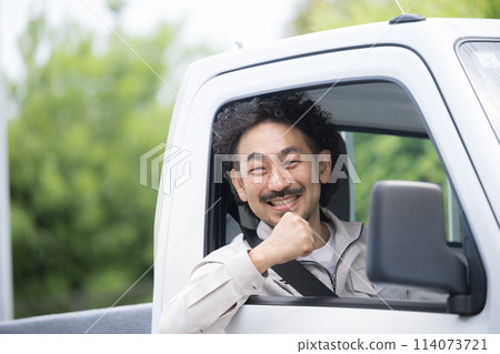 A middle-aged man in work clothes driving a truck among fresh greenery, looking at the camera, fist pump, image of transportation and delivery industry A middle-aged man in work clothes driving a truck among fresh greenery, looking at the camera, fist pump, image of transportation and delivery industry 114073721