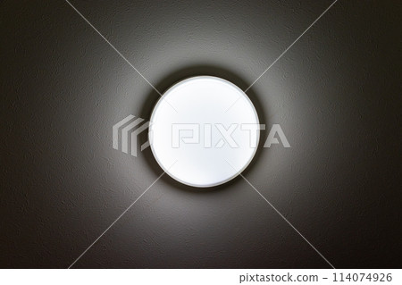 A circular light fixture glowing on the ceiling of a dark room A circular light fixture glowing on the ceiling of a dark room 114074926