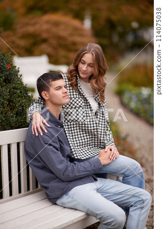 Autumn Romance: Young Couple Embracing and Kissing on Park Bench. Young couple kissing and rejoices at the lake. lovely young couple kissing outdoors in autumn. Embraced in Autumn's Warmth: Couple's 114075038