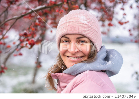 Winter Elegance: Portrait of a Beautiful Girl in a Snowy European Village. Winter lifestyle portrait of cheerful pretty girl. Smiling and having fun in the snow park. Snowflakes falling down 114075049