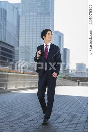 A businessman in his 30s walking through a business district 114076592