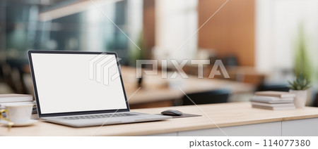 A laptop computer on a minimal wood table with a blurred background of a modern meeting room. 114077380