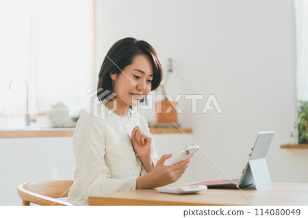 Image of a housewife in her 40s with a frozen smile as she looks at her smartphone screen 114080049