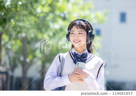 A high school girl wearing headphones and holding a smartphone A high school girl wearing headphones and holding a smartphone 114081857
