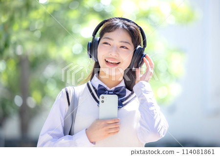 A high school girl wearing headphones and holding a smartphone 114081861