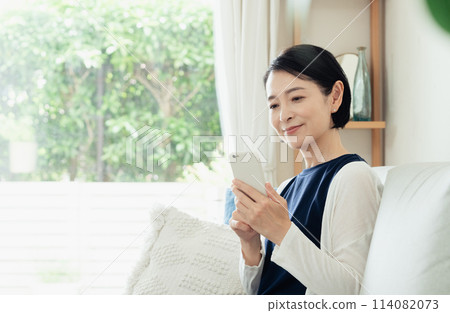 A housewife operating a smartphone in the living room A housewife operating a smartphone in the living room 114082073