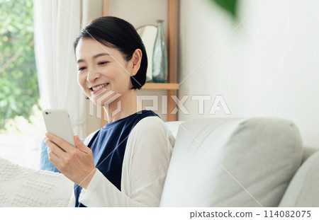 A housewife operating a smartphone in the living room A housewife operating a smartphone in the living room 114082075