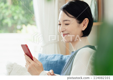 在客廳操作智慧型手機的家庭主婦 114082101