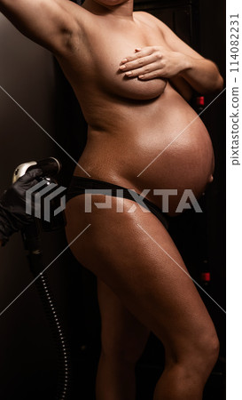 The master evens out an instant tan with a brush on the skin of a pregnant woman. Close-up of the tummy. The master evens out an instant tan with a brush on the skin of a pregnant woman. Close-up of the tummy. 114082231