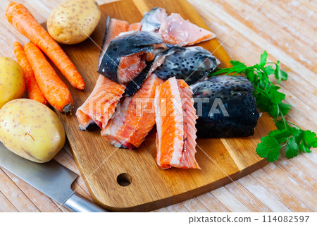 There are salmon trimmings on cutting board - head, spine, tail with potatoes, carrots, parsley There are salmon trimmings on cutting board - head, spine, tail with potatoes, carrots, parsley 114082597