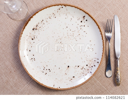 In eating-house on table round plate with cutlery, knife and fork complemented by transparent glass 114082621