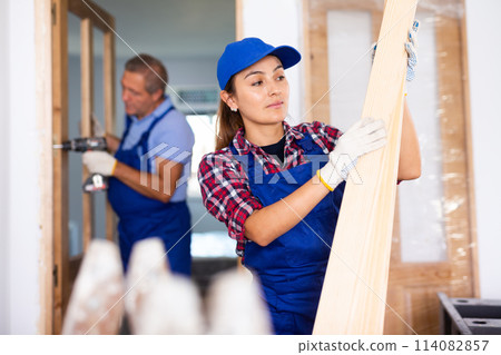 Positive Latin female carpenter in uniform holding wooden planks indoors Positive Latin female carpenter in uniform holding wooden planks indoors 114082857