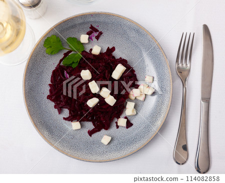 On plate is portion of salad of grated boiled beetroot with addition of small pieces of white cheese. 114082858
