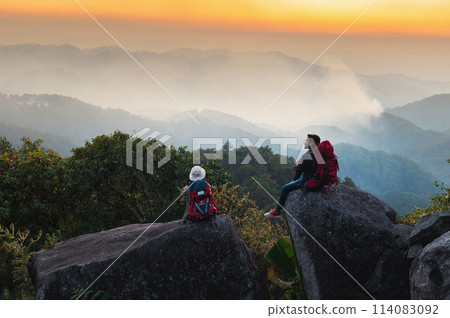 man and a woman are sitting on a rock overlooking a mountain range 114083092