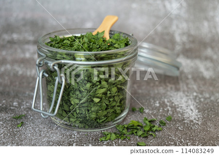 Dry parsley spice with wooden spoon in glass jar. Homegrown herbs and spices for cooking. Fresh dried aromatic natural food ingredients 114083249
