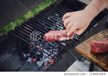 Unrecognizable man put raw steak on grill Unrecognizable man put raw steak on grill 114083869