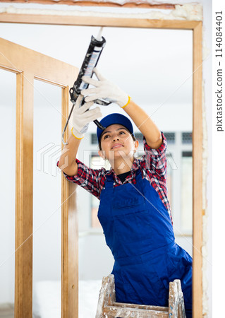 Experienced female door installer fills gaps with mounting foam Experienced female door installer fills gaps with mounting foam 114084401