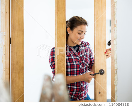 Cheerful woman installing door handle 114084518