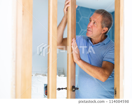 Ordinary elderly man checks the quality of the installed wooden door 114084598