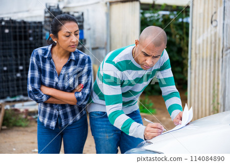Woman and man discussing documents on farm near car 114084890