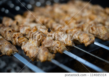 Person grilling brochettes of meat on skewers outdoors for a delicious meal 114085314