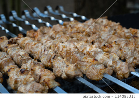Person grilling brochettes of meat on skewers outdoors for a delicious meal Person grilling brochettes of meat on skewers outdoors for a delicious meal 114085315