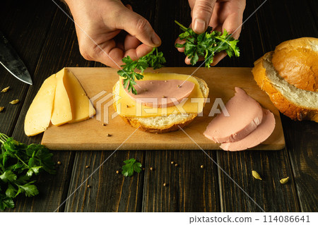 Preparing a sandwich in a restaurant on the kitchen table. The chef hand adds fresh parsley to the sandwich. Advertising space Preparing a sandwich in a restaurant on the kitchen table. The chef hand adds fresh parsley to the sandwich. Advertising space 114086641