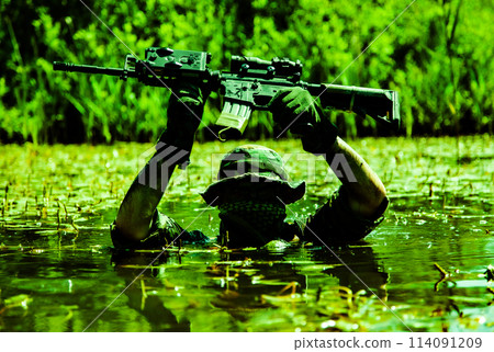 A soldier moves in the heart of a marsh, submerged in swampy waters with only arms and rifle visible, extreme conditions of concealed tactical combat operations of special task forces 114091209