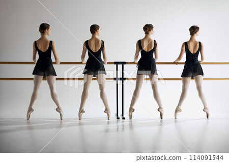 Showing precision. Young girls, ballet dancers in black costumes standing at barre, practicing moves against grey studio background 114091544