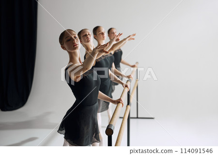 Ballet practice at barre. Beautiful young girl, ballet dancers in black costumes training, preparing for performance against grey studio background Ballet practice at barre. Beautiful young girl, ballet dancers in black costumes training, preparing for performance against grey studio background 114091546