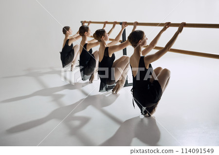 Discipline and determination. Tender teen girls, ballet dancers in black costumes attending dance class, training against grey studio background Discipline and determination. Tender teen girls, ballet dancers in black costumes attending dance class, training against grey studio background 114091549