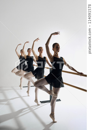 Dynamic ballet sequence. Elegant teen girls, ballet dancers standing at barre, practicing movements against grey studio background Dynamic ballet sequence. Elegant teen girls, ballet dancers standing at barre, practicing movements against grey studio background 114091578