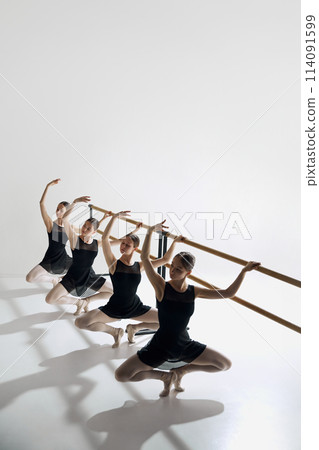 Elegance in training. Beautiful, focused teen girls, ballet dancers standing at barre and practicing against grey studio background 114091599