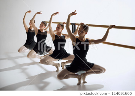 Elegance in training. Beautiful, focused teen girls, ballet dancers standing at barre and practicing against grey studio background Elegance in training. Beautiful, focused teen girls, ballet dancers standing at barre and practicing against grey studio background 114091600